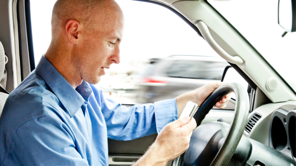 Man looking down at cellphone while driving shows the dangers of distractions while driving.