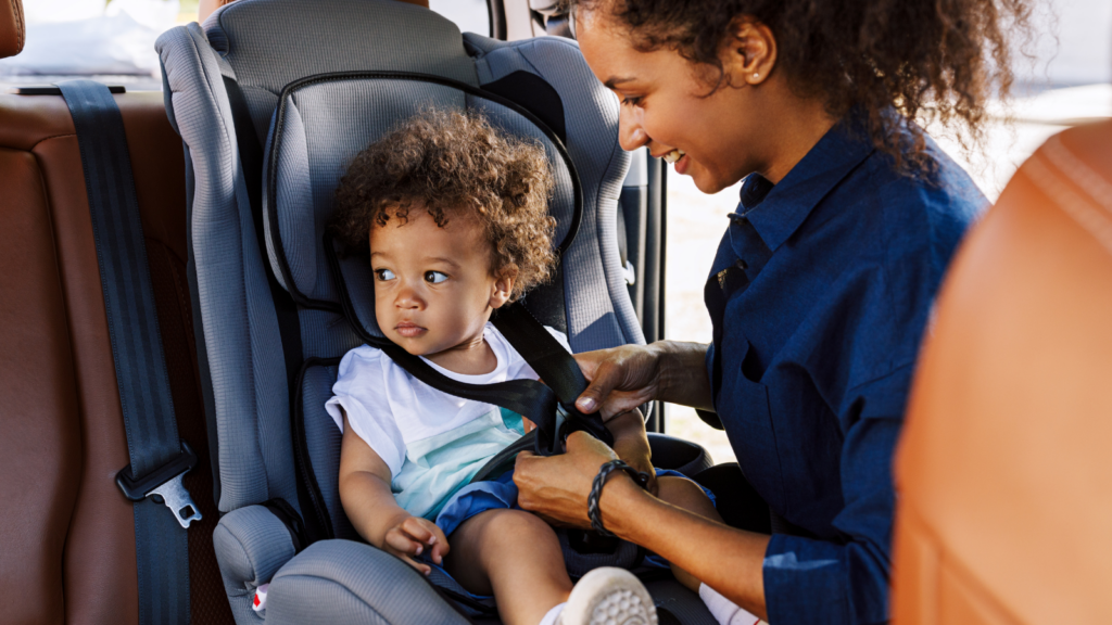 Mom buckling in her child into the car to protect child in their carseat.