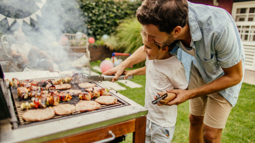 Dad helps child while grilling which shows the importance of fire safety.